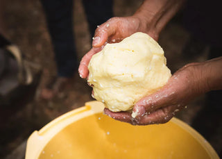 Zwei Hände formen frisch hergestellte Butter über einem Eimer mit Buttermilch – traditionelle Butterherstellung von Hand