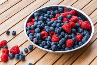 Frische Heidelbeeren und Himbeeren in einer Schale auf hellem Holztisch – Früchte als Teil der täglichen Vitaminzufuhr